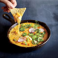 someone is dipping some tortilla into a skillet filled with cheese and veggies