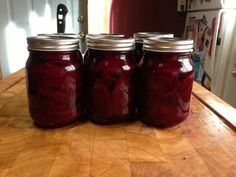 four jars filled with pickles sitting on top of a wooden table