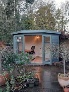 a small garden shed in the middle of a yard with potted plants and trees