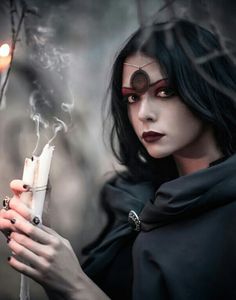 a woman holding a lit candle in her right hand and wearing black clothing with red eyes