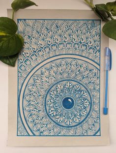 a blue and white drawing on top of a piece of paper next to a pen