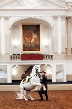 a man standing next to a white horse in a room with paintings on the walls