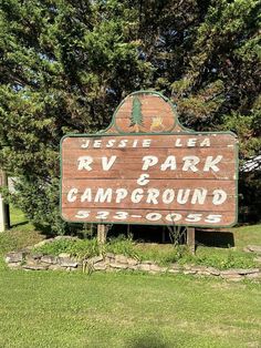 a wooden sign sitting in the middle of a lush green field next to a forest