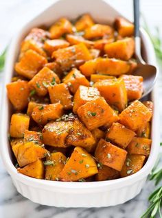 a white casserole dish filled with roasted sweet potatoes and garnished with herbs