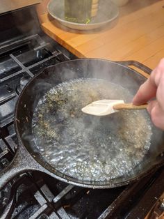 a person stirring something in a frying pan on top of the stove with a wooden spoon