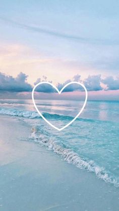 a heart drawn in the sand on a beach with waves coming up to shore and blue sky