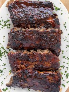 baby back ribs on a white plate with parsley and text overlay that reads oven baked fall off the bone baby back ribs