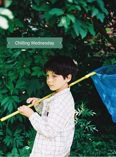 a young boy holding a blue umbrella in front of some trees and bushes with the words chilling wednesday on it