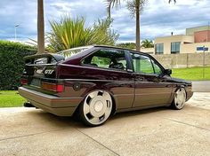 a maroon car parked on the side of a road next to palm trees and bushes