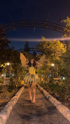 a woman dressed in a fairy costume walking down a path at night with her hands on her hips