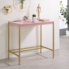 a pink and gold console table against a white wall with potted plants on it