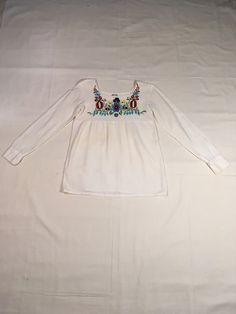 "vintage 1970s pullover blouse hand woven, made in India white cotton gauze w/ colorful floral embroidery across chest square neck long sleeve w/2 snap cuff good vintage condition, light wear small repair and underside patch to right underarm small green smudge on right sleeve (see last photos) measures, lying flat, shoulder-16\" chest-17 1/2\" sleeve-24\" hem-21\" length-27\"" Cotton Long Sleeve Blouse With Floral Embroidery, Multicolor Long Sleeve Bohemian Blouse, Multicolor Bohemian Long Sleeve Blouse, Bohemian Multicolor Long Sleeve Blouse, Spring Bohemian Crew Neck Blouse, Casual Long Sleeve Embroidered Blouse, Long Sleeve Tops With Floral Embroidery For Summer, Casual White Blouse With Boho Collar, Fitted Long Sleeve Peasant Top For Festival