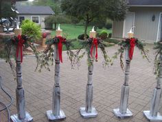 four candles decorated with evergreen and red bows are lined up on the side of a brick walkway