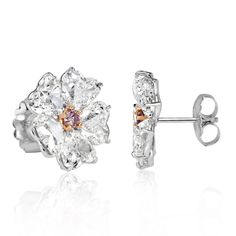 These 18k white gold diamond earring studs are feminine and truly one-of-a-kind. This design showcases 10.64ct of diamonds that are certified at G-I colors and VS2-SI2 clarities. The stunning heart shaped diamonds are styled as floral petals that are individually GIA certified, weighing in at just over 1 carat each. In the center of the design is a rare fancy pink diamond that is secured by rose gold prongs. These beauties are not only extremely unique but posess a beautiful allure that will mes