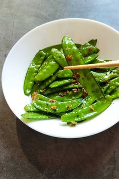 a white bowl filled with green beans and chopsticks