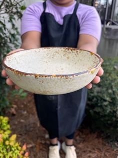 a person holding a white bowl in their left hand and wearing an apron on the other