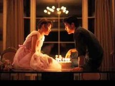 a man and woman sitting at a table in front of a cake with lit candles