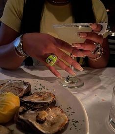 a woman sitting at a table with oysters in front of her and a drink