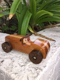 a small wooden toy car sitting on top of a stone wall next to green plants