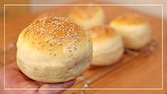 a person holding a bun with sesame seeds on it in front of other buns