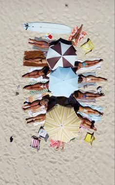 a group of people laying on top of a sandy beach under an umbrella covered in sunshades