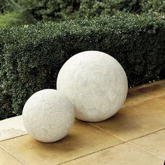 two white balls sitting next to each other on top of a cement slab in front of bushes