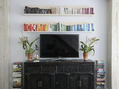 a flat screen tv sitting on top of a wooden cabinet next to a book shelf filled with books