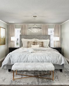 a bedroom with a bed, ottoman and chandelier