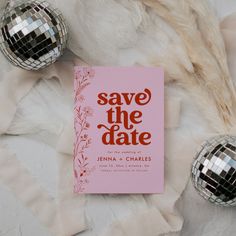 a pink save the date book sitting on top of a bed next to two disco balls