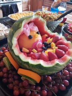 a watermelon shaped like a baby in a fruit bowl with grapes and strawberries