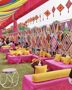 an outdoor event with bright colored decorations and tables covered in pink linens, yellow pillows and colorful streamers