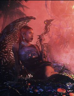 a woman sitting on the ground in front of an alien like creature with her arm outstretched