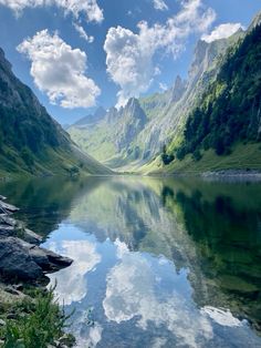 the mountains are reflected in the still water on the lake's edge, while clouds hover above them