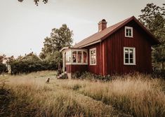 a red house sitting in the middle of a field with tall grass and trees around it