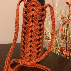 an orange crocheted bag sitting on top of a table next to a vase