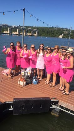 a group of women in pink dresses standing on a dock