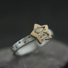 a silver and gold ring with two small diamonds on the front, sitting on top of a rock