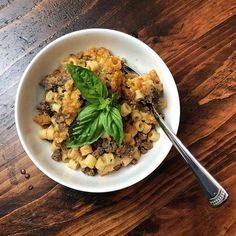 a white bowl filled with food on top of a wooden table next to a fork