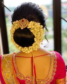 the back of a woman's head with flowers in her hair and an elaborate necklace