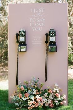 two old fashioned telephones sitting on top of a pink wall next to some flowers