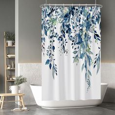 a white shower curtain with blue and green leaves on it next to a bathtub