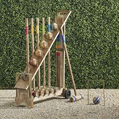 a wooden toy set with baseballs, bats and balls in front of a hedge