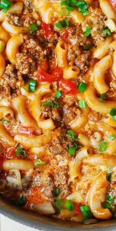 a skillet filled with pasta and meat covered in sauce, green onions and parsley