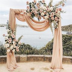 an outdoor wedding setup with pink drapes and flowers on the arch over looking the water