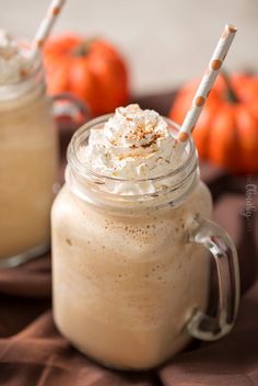 two mason jars with whipped cream and pumpkins in the background