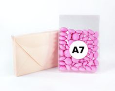 pink candy pebbles in a clear plastic container next to an envelope on a white background