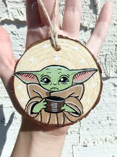 a hand holding a wooden ornament with an image of baby yoda on it