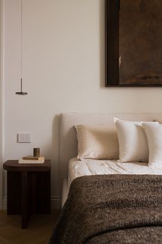 a bed with white and brown pillows in a bedroom next to a painting on the wall