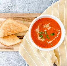 a bowl of tomato soup with bread on a cutting board next to it and a napkin