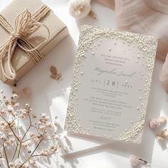 a white wedding card with pearls on it next to some flowers and a gift box